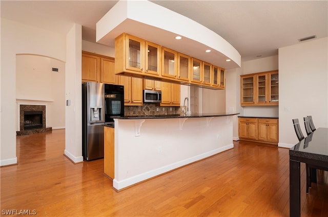 kitchen featuring sink, a breakfast bar area, decorative backsplash, appliances with stainless steel finishes, and light wood-type flooring