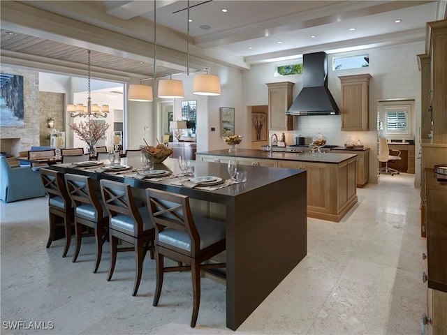 kitchen featuring beam ceiling, hanging light fixtures, wall chimney range hood, a notable chandelier, and a spacious island