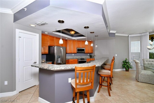 kitchen featuring kitchen peninsula, pendant lighting, a breakfast bar area, appliances with stainless steel finishes, and ornamental molding