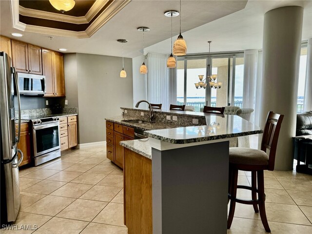 kitchen with a raised ceiling, crown molding, hanging light fixtures, dark stone countertops, and stainless steel appliances