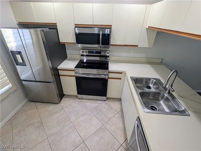 kitchen with white cabinets, appliances with stainless steel finishes, light tile patterned floors, and sink