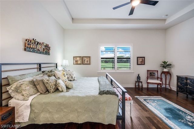 bedroom with dark hardwood / wood-style flooring, ceiling fan, and a tray ceiling