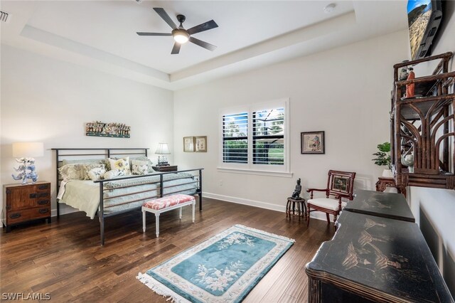 bedroom with ceiling fan, dark hardwood / wood-style flooring, and a tray ceiling