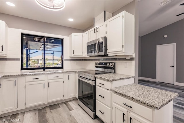 kitchen with stainless steel appliances, sink, white cabinets, decorative backsplash, and light stone countertops