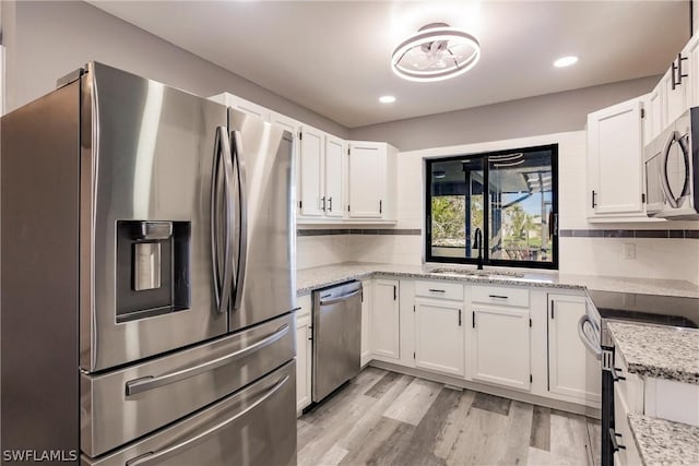 kitchen with stainless steel appliances, white cabinetry, light stone counters, light hardwood / wood-style floors, and decorative backsplash