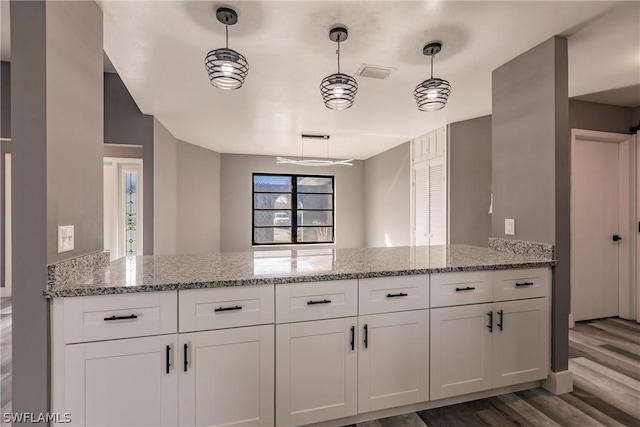 kitchen with light stone counters, kitchen peninsula, hanging light fixtures, hardwood / wood-style floors, and white cabinetry