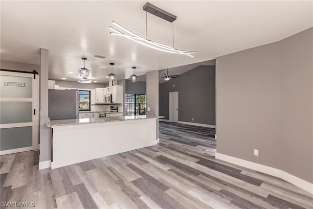 kitchen with light stone counters, hanging light fixtures, a barn door, white cabinets, and appliances with stainless steel finishes