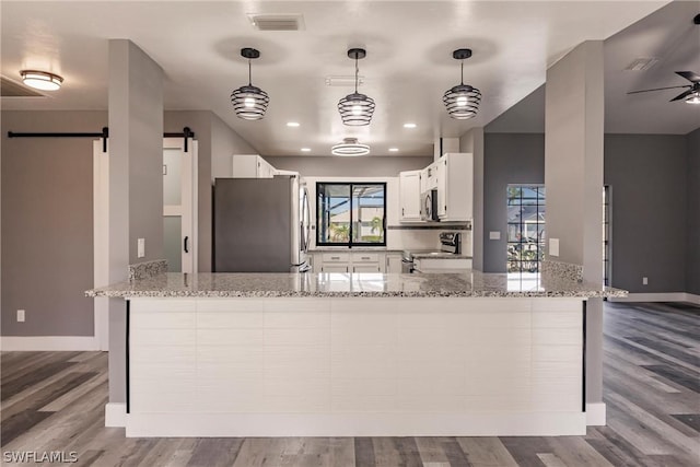 kitchen featuring a barn door, stainless steel appliances, light stone countertops, kitchen peninsula, and white cabinets