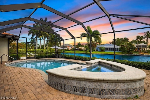 pool at dusk featuring glass enclosure, a water view, and an in ground hot tub