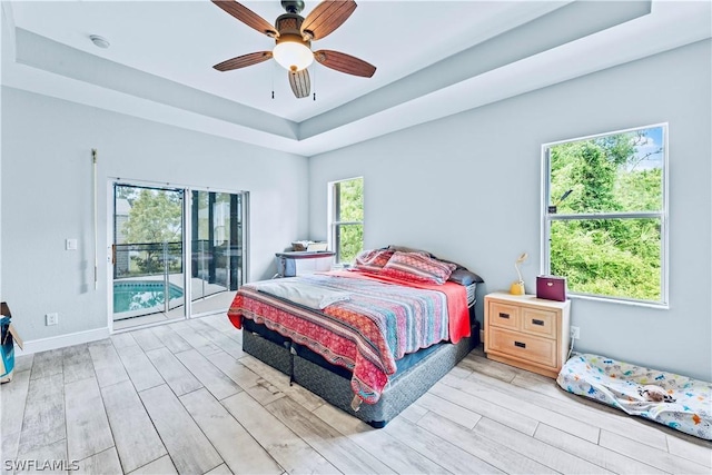 bedroom featuring access to exterior, a raised ceiling, light hardwood / wood-style flooring, and ceiling fan