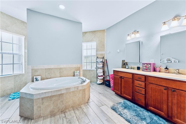 bathroom with tiled bath, vanity, hardwood / wood-style flooring, and a wealth of natural light