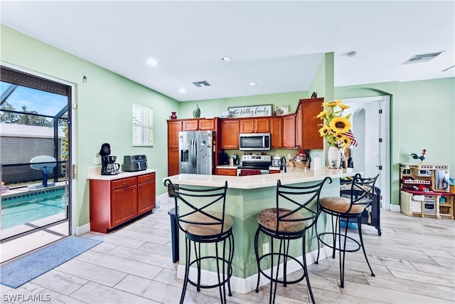 kitchen featuring a kitchen breakfast bar, light hardwood / wood-style floors, kitchen peninsula, and appliances with stainless steel finishes