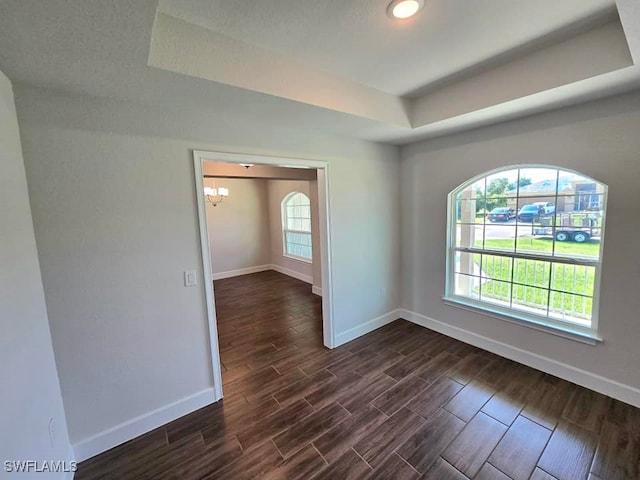 spare room featuring a tray ceiling, a healthy amount of sunlight, dark hardwood / wood-style flooring, and a chandelier