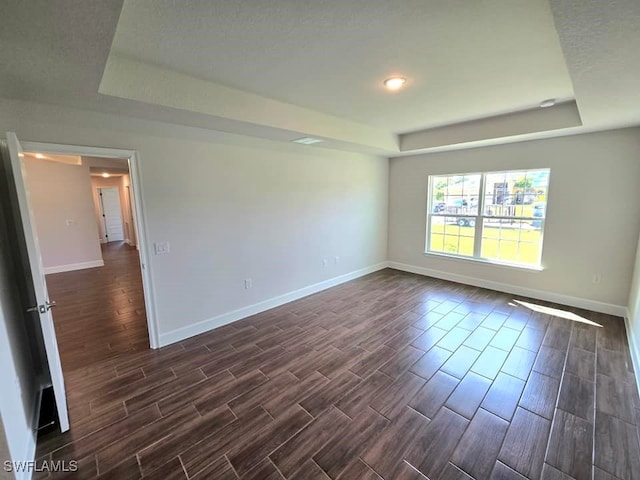 unfurnished room featuring a textured ceiling, a tray ceiling, and dark hardwood / wood-style flooring