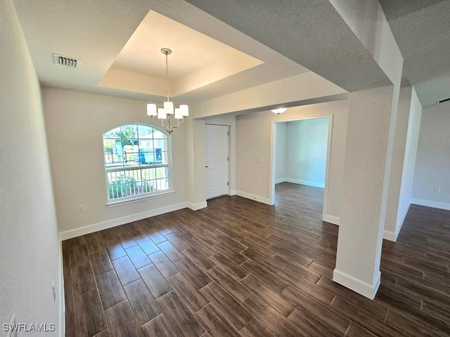 unfurnished dining area featuring a textured ceiling, dark hardwood / wood-style floors, a chandelier, and a raised ceiling