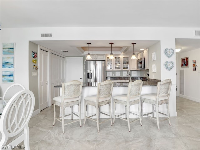 kitchen featuring a raised ceiling, dark stone countertops, appliances with stainless steel finishes, decorative light fixtures, and kitchen peninsula