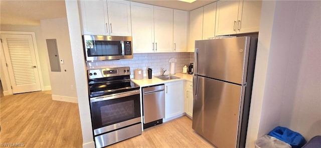 kitchen featuring decorative backsplash, stainless steel appliances, white cabinetry, and light hardwood / wood-style floors