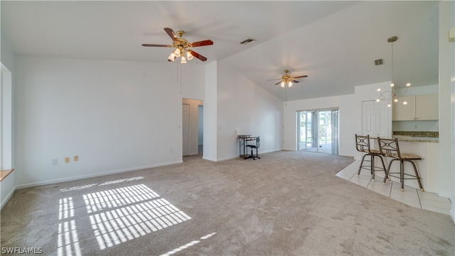 unfurnished living room with light colored carpet, high vaulted ceiling, and ceiling fan with notable chandelier