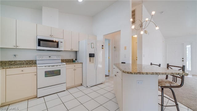 kitchen featuring a kitchen breakfast bar, light stone countertops, white appliances, and light tile flooring