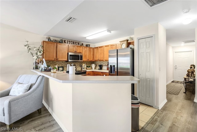 kitchen featuring light hardwood / wood-style flooring, kitchen peninsula, stainless steel appliances, and tasteful backsplash