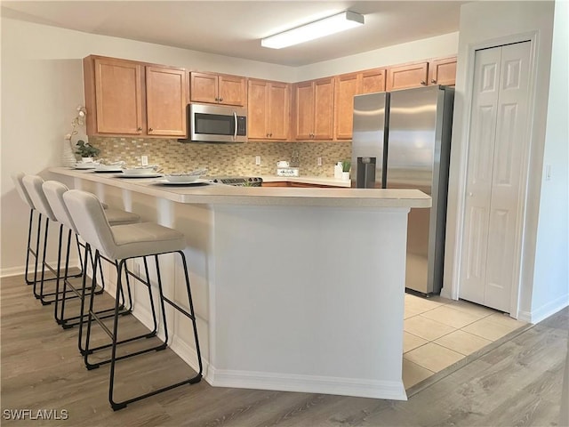 kitchen featuring tasteful backsplash, a kitchen breakfast bar, kitchen peninsula, stainless steel appliances, and light hardwood / wood-style flooring