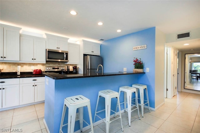 kitchen featuring stainless steel appliances, backsplash, a kitchen bar, white cabinetry, and light tile floors