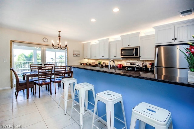 kitchen with stainless steel appliances, a notable chandelier, hanging light fixtures, tasteful backsplash, and white cabinets