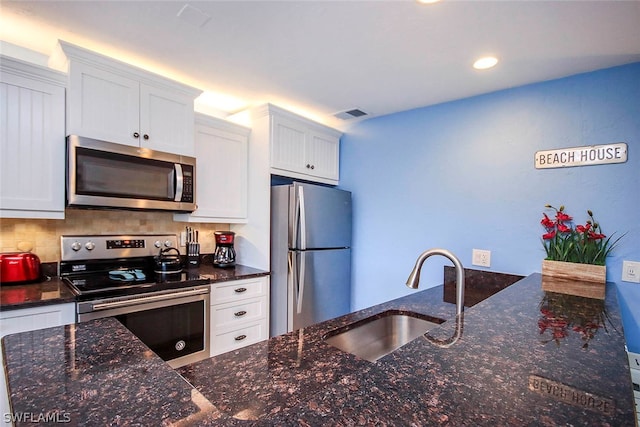 kitchen featuring dark stone countertops, stainless steel appliances, white cabinets, backsplash, and sink