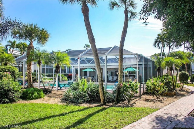 rear view of house featuring glass enclosure, an outdoor pool, and a yard