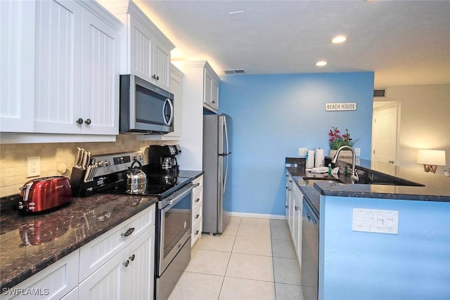 kitchen with light tile patterned floors, decorative backsplash, dark stone counters, stainless steel appliances, and a sink