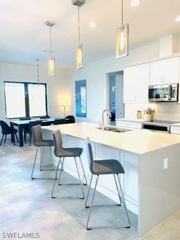 kitchen with a kitchen breakfast bar, a center island with sink, white cabinets, and pendant lighting