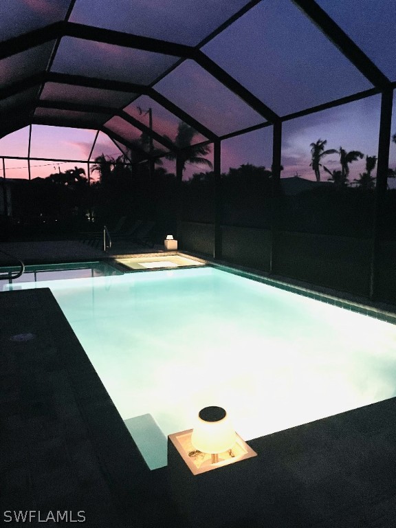 pool at dusk with a lanai and a patio