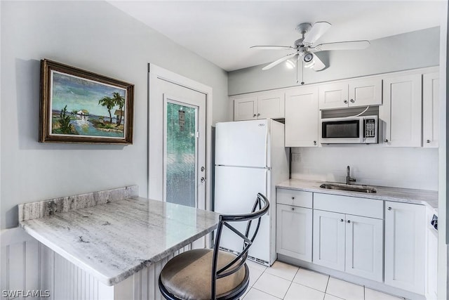 kitchen with stainless steel microwave, a peninsula, freestanding refrigerator, white cabinetry, and a sink