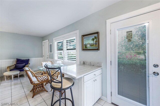 kitchen featuring light stone counters, white cabinets, a breakfast bar area, and light tile floors