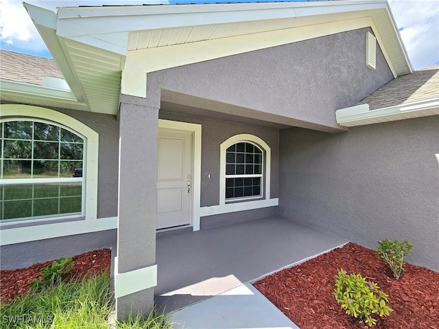 doorway to property featuring stucco siding and roof with shingles