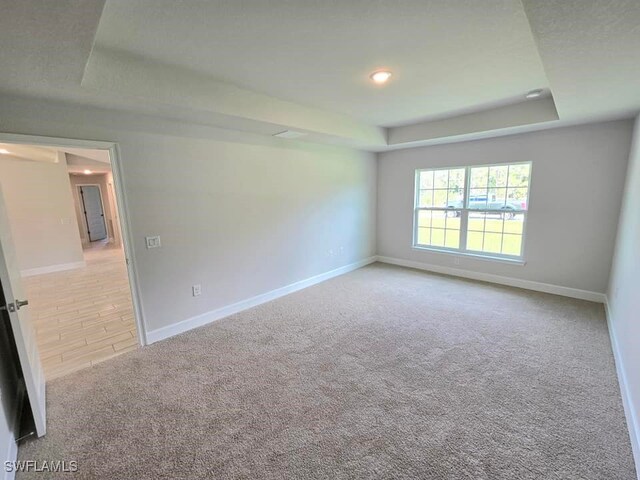 carpeted spare room featuring baseboards and a raised ceiling