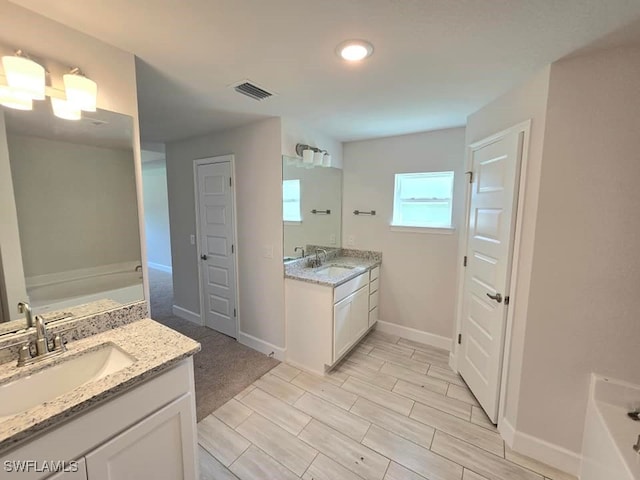 bathroom with a garden tub, two vanities, visible vents, and a sink