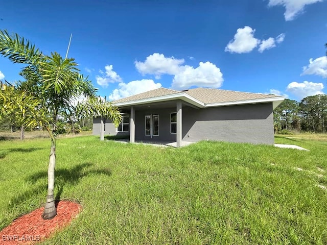 back of property featuring stucco siding, a yard, and roof with shingles