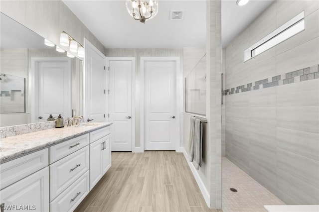 bathroom featuring hardwood / wood-style floors, vanity, tiled shower, and an inviting chandelier