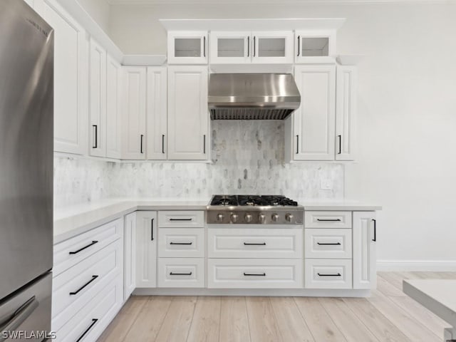 kitchen with appliances with stainless steel finishes, tasteful backsplash, white cabinetry, and wall chimney range hood