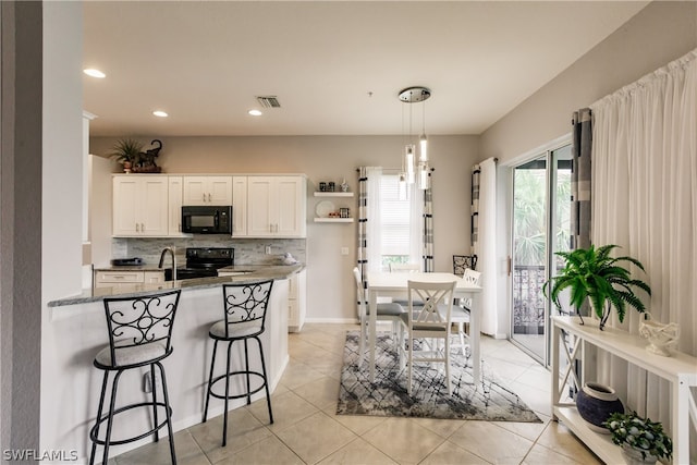 kitchen with hanging light fixtures, tasteful backsplash, black appliances, white cabinets, and light tile floors