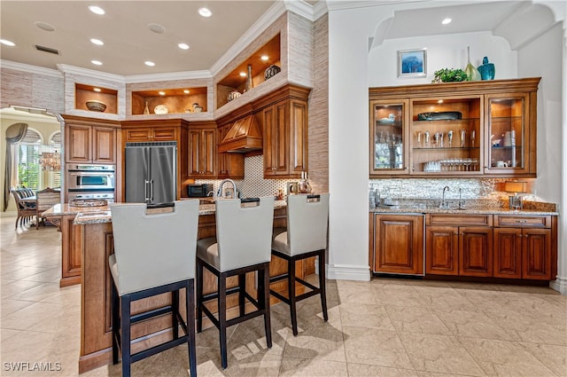 kitchen featuring light stone countertops, a kitchen bar, custom exhaust hood, stainless steel appliances, and crown molding