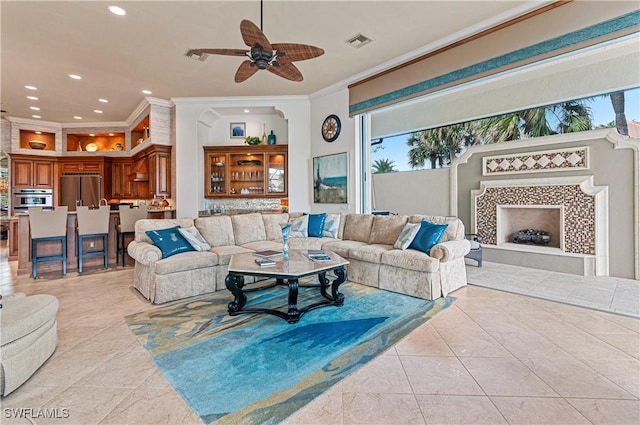 living room with ceiling fan, ornamental molding, a fireplace, and light tile patterned floors