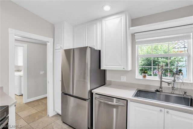 kitchen with appliances with stainless steel finishes, sink, washer / dryer, white cabinetry, and lofted ceiling