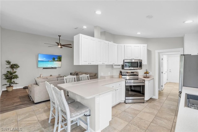 kitchen with appliances with stainless steel finishes, a breakfast bar, white cabinets, ceiling fan, and kitchen peninsula