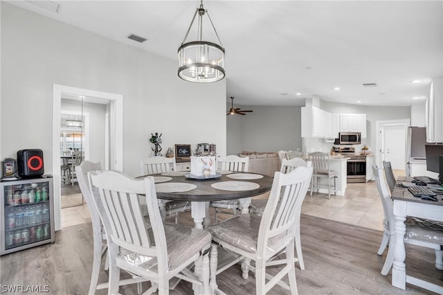 dining space featuring wine cooler, ceiling fan with notable chandelier, and light hardwood / wood-style floors