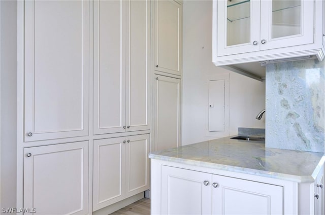 kitchen with white cabinets, light hardwood / wood-style flooring, light stone countertops, and sink