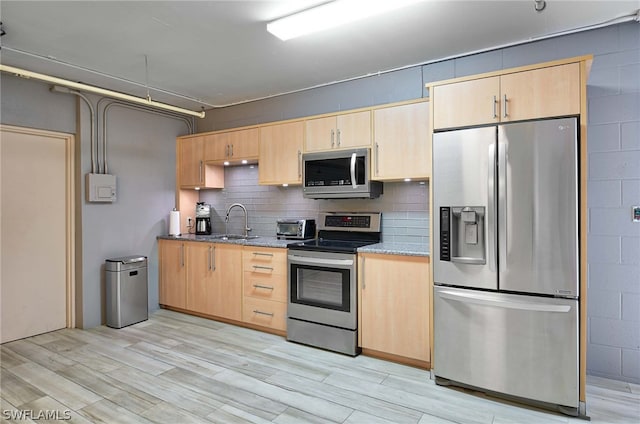 kitchen with light brown cabinetry, light wood-type flooring, stainless steel appliances, sink, and dark stone countertops