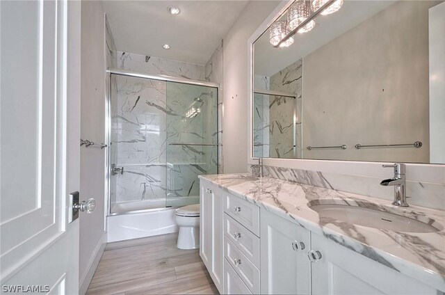 full bathroom featuring wood-type flooring, vanity, bath / shower combo with glass door, and toilet