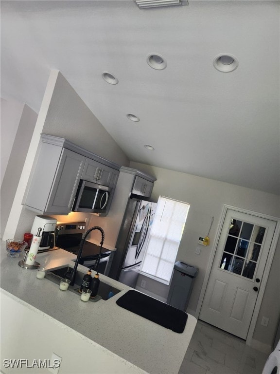 kitchen featuring kitchen peninsula, stainless steel appliances, gray cabinets, and lofted ceiling